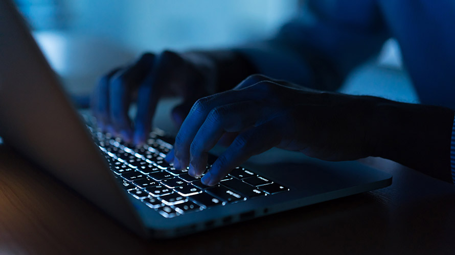 Mãos de pessoa utilizando o teclado de um notebook, com iluminação escura no ambiente